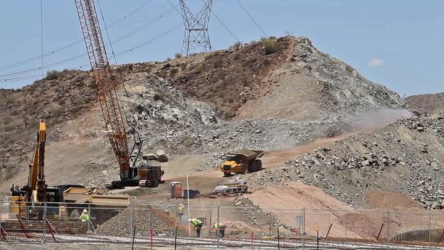 Heavy equipment, Cranes, Dump Trucks and works on a mountainside road building project.