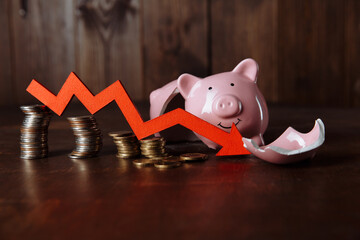 Broken piggy bank and red arrow down with coins stack. Investment and bankruptcy concept