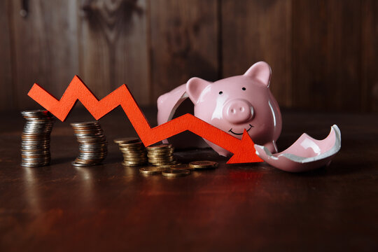 Broken piggy bank and red arrow down with coins stack. Investment and bankruptcy concept