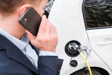 Man charging an electric car and talking on the smartphone. Eco EV car concept