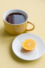 top view of a yellow cup of coffee or tea on a yellow background and a lemon on a white plate, black tea to treat and get rid of the symptoms of the common cold and coronovirus
