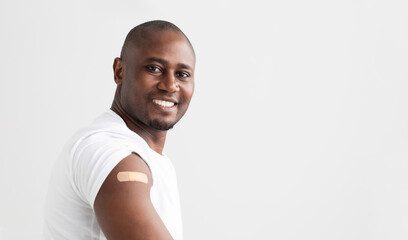 Covid-19 vaccination. Smiling african american man showing his arm with an adhesive bandage, copy...