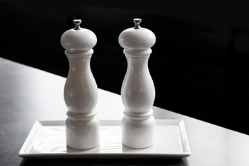 White pepper shaker and white salt shaker on a dark background