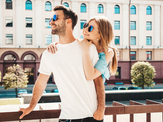 Portrait of smiling beautiful woman and her handsome boyfriend. Woman in casual summer jeans dress. Happy cheerful family. Female having fun. Couple posing on the street background in sunglasses