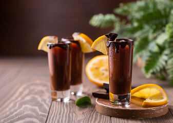 Cocktail in shot glass with chocolate, cream liqueur, fresh oranges on dark background. Homemade shot drinks party. Bar menu, recipes.