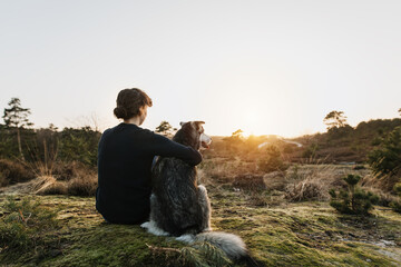 Person hugging a dog outdoors in beautiful nature. They enjoy the sunset. Emotional connection with trust. Happy content time together. Friendship between humans and dogs. Hugs.