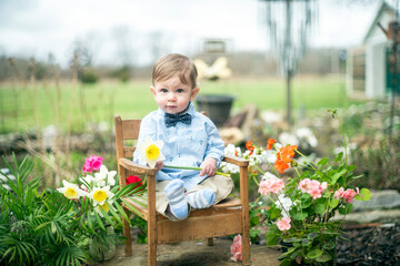 Cute baby boy sitting in bowtie sitting with flowers outdoors on farm for spring or Easter