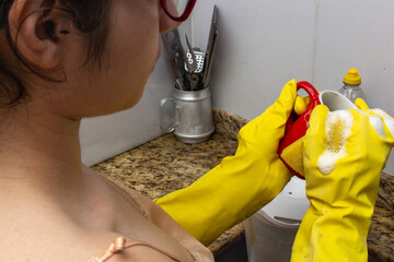 Woman in kitchen with yellow gloves washing red cup