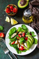 Healthy food, diet lunch menu concept, ketogenic diet and paleodiet. Summer salad with strawberries, grilled chicken and avocado on a stone table. Top view flat lay.