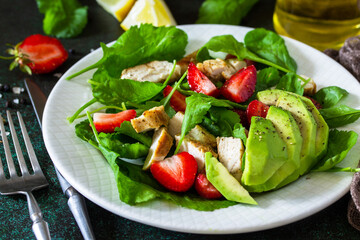 Healthy food, diet lunch menu concept, ketogenic diet and paleodiet. Summer salad with strawberries, grilled chicken and avocado on a stone table.