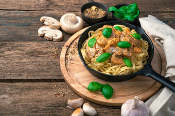 Frying pan with pasta with mushroom sauce on a cutting board with a background of mushrooms and garlic.