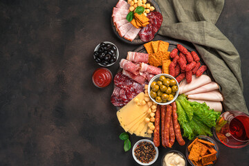 Charcuterie board. Different types of sausages, cheese, lettuce and olives on a brown background.