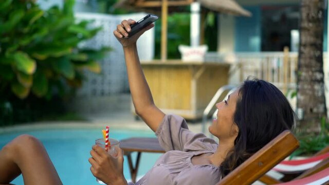Woman with cocktail taking selfie photo with smartphone by the pool