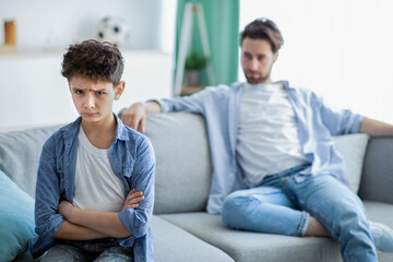 Family generations conflict. Upset boy and father not talking after quarrel, son and dad sitting on...