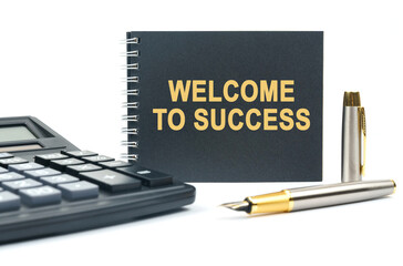 On a white background, there is a calculator, a pen and a black notebook with the inscription - WELCOME TO SUCCESS