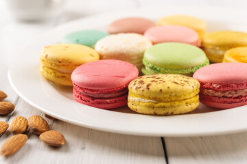 Closeup of tasty multicolored macaroons on a white porcelain plate. Sweet breakfast with delicious almond meringue cookies. Colorful macaron cake dessert. Selective focus.