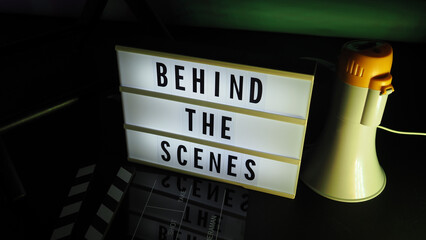 Behind the scenes light box. Text on cinema light box. Megaphone and director chair and movie slate beside. Background LED color. Camera in video production studio. Behind the scene concept.