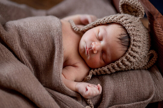 Newborn baby, beautiful infant lies in brown fur blanket on wood background, 10 days old girl sleeping in the bed. Copy space