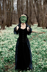 romantic girl in vintage dress with a mirror on meadow with snowdrops in the forest