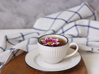 A cup of tea and a flower. A cup on a wooden tray and a checked towel. Spring concept. Tenderness and femininity