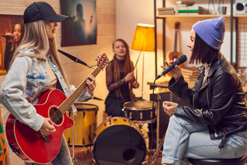 Fototapeta premium Group of young women singing and playing musical instruments during rehearsal in the studio