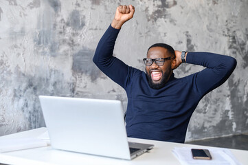 Emotional young african-american man looking at laptop screen, celebrating winning long-awaited game or getting price in online lottery, reading message with unbelievable pleasant news, got promoted
