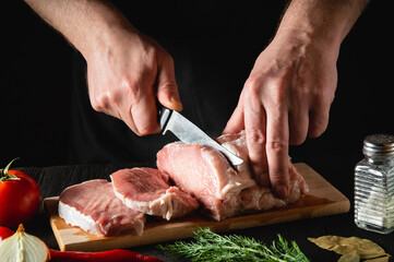 Chef Butcher cutting pork meat with knife on kitchen, cooking food. Vegetables and spices on the kitchen table to prepare delicious lunch