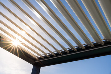 Trendy outdoor patio pergola. the sun's rays pass through the metallic structure - obrazy, fototapety, plakaty