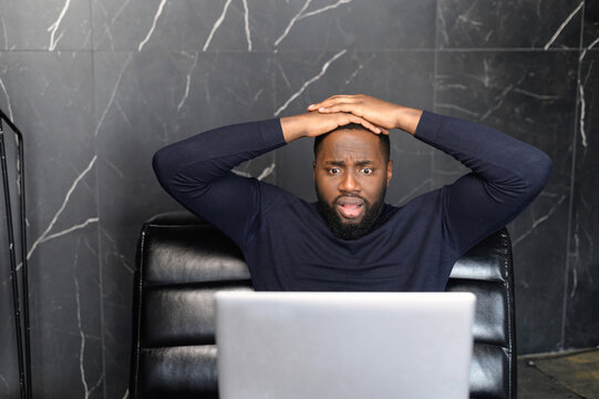 Oh no. Portrait of shocked black businessman holding hands on head, looking very disappointed, looking at screen of computer eyes wide open, thinking received bad news, waiting hoping positive result