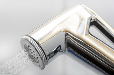 A chrome bidet shower spraying water, close up. The head of the toilet bidet.