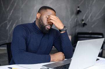 Difficult task from customer. African American man conducts correspondence using a laptop, hearing...