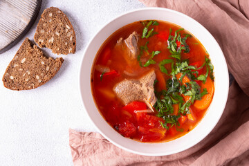 Turkish cuisine. Shurpa soup in a round plate and bread on a pink cloth. Flat lay.