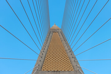 Concrete bridge pylon with parallel lines of steel cable. Passage under the supporting tower of the cable bridge. Construction Cable-stayed bridge against blue sky.