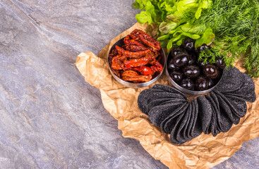 Black chips with olives and tomatoes. Chips and herbs  copy space