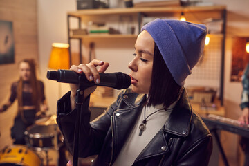 Female singer singing in microphone and rehearsing with her colleagues in the studio