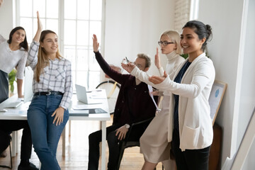 Fototapeta premium Smiling multiracial colleagues coworkers engaged in teambuilding activity at meeting in office. Happy confident Indian female team leader hold briefing, interact with diverse employees at workplace.