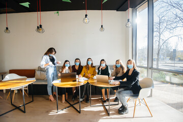 Fototapeta na wymiar A group of girls in masks sit in a cafe and work on laptops. Teaching students.