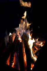 wooden logs burn with a bright yellow-red flame against the background of the night, sparks fly off the fire
