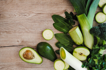 Green vegetables and fruits lie on a wooden table. Broccoli, leeks, apple and avocado.