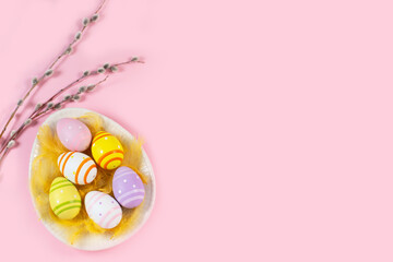 Easter colorful eggs in an egg-shaped plate with willow twigs on light background.