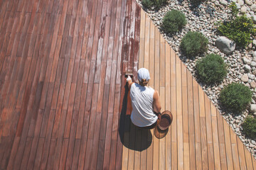 Wood deck renovation treatment, the person applying protective wood stain with a brush, overhead...