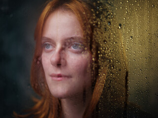Red-haired girl near a rainy window