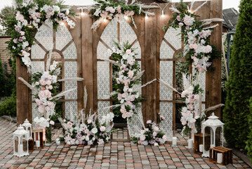Fototapeta na wymiar Rustic wooden wedding arch with retro garland decorated with flowers for wedding ceremony newlyweds