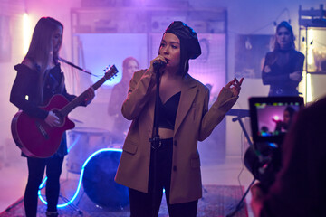 Female singer singing in microphone and performing together with her group and recording their...