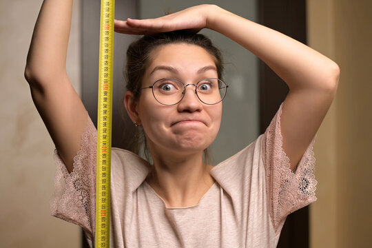 A young woman shows joy at her growth by holding a measuring tape next to her