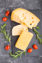 Various types of cheese with rosemary and tomatoes on black slate board on a black concrete...