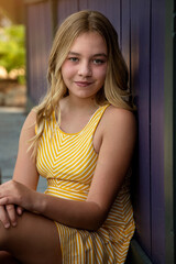 Vertical outdoor portrait of a beautiful tween girl with long blonde hair wearing a yellow dress...