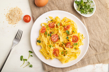 Reginelle semolina pasta with tomato, eggs, sesame and microgreen sprouts on a white wooden background. Top view, close up.