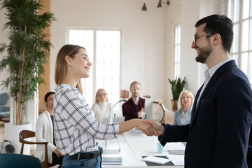 Smiling businessman handshake excited young Caucasian woman worker congratulate with promotion or...
