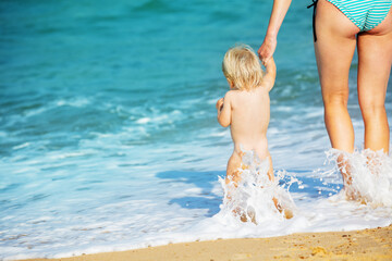 Mother and little toddler walk in the sea waves